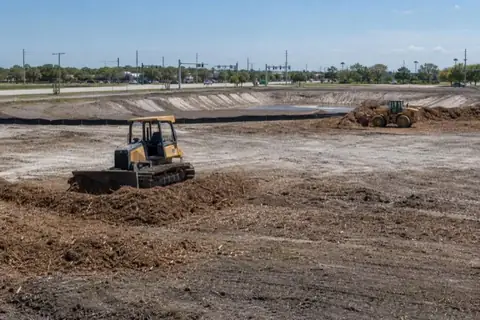 Two machines clearing a silt-fenced commercial parcel along a Port St. Lucie arterial