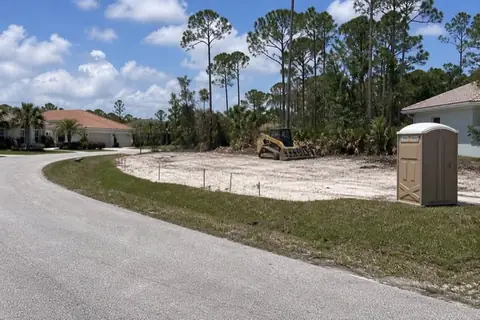 Partly cleared infill lot with survey stakes between occupied Port St. Lucie homes
